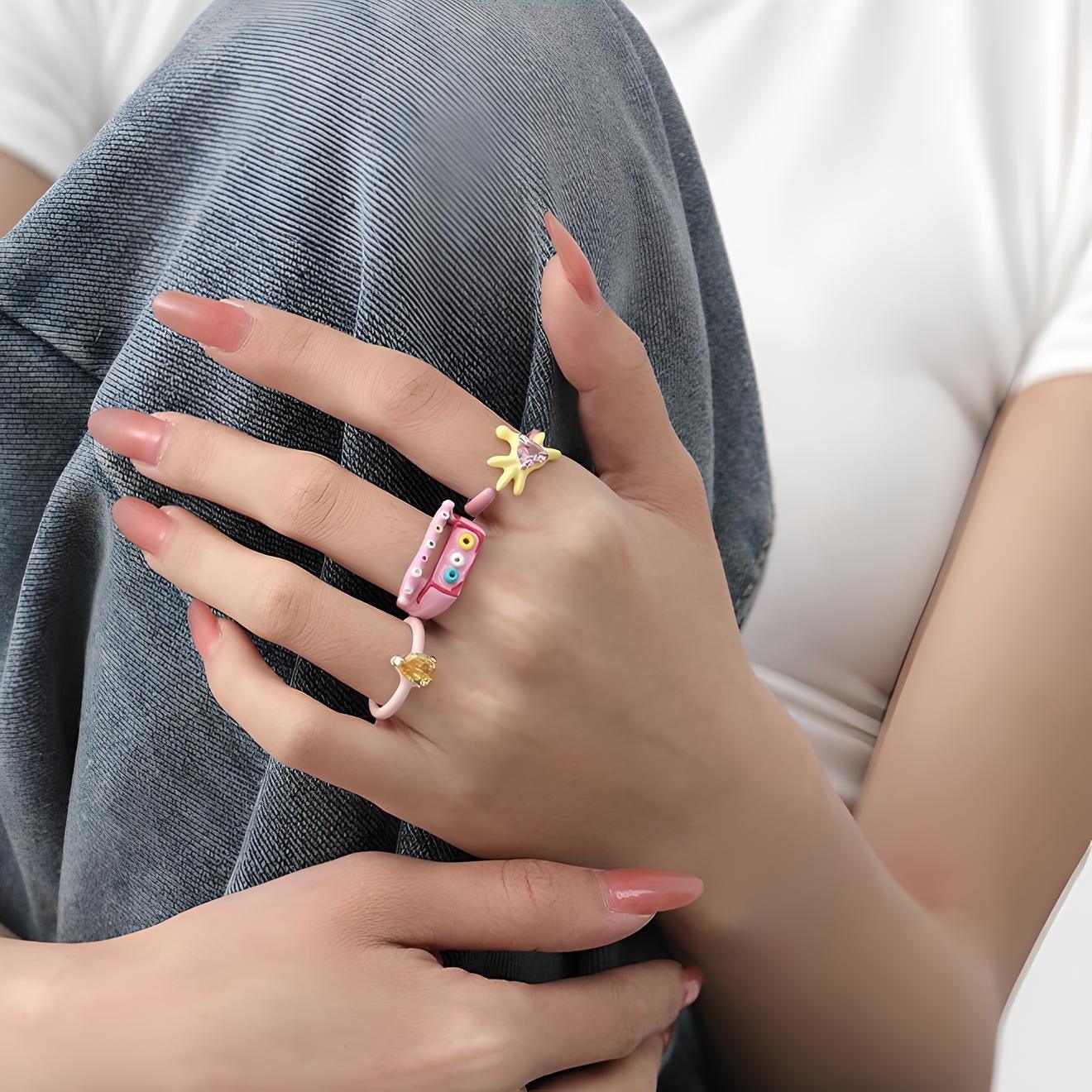 Close-up of a woman's hand with manicured nails wearing a colorful, whimsical ring, resting on her denim-clad knee, accentuating a casual yet stylish look.