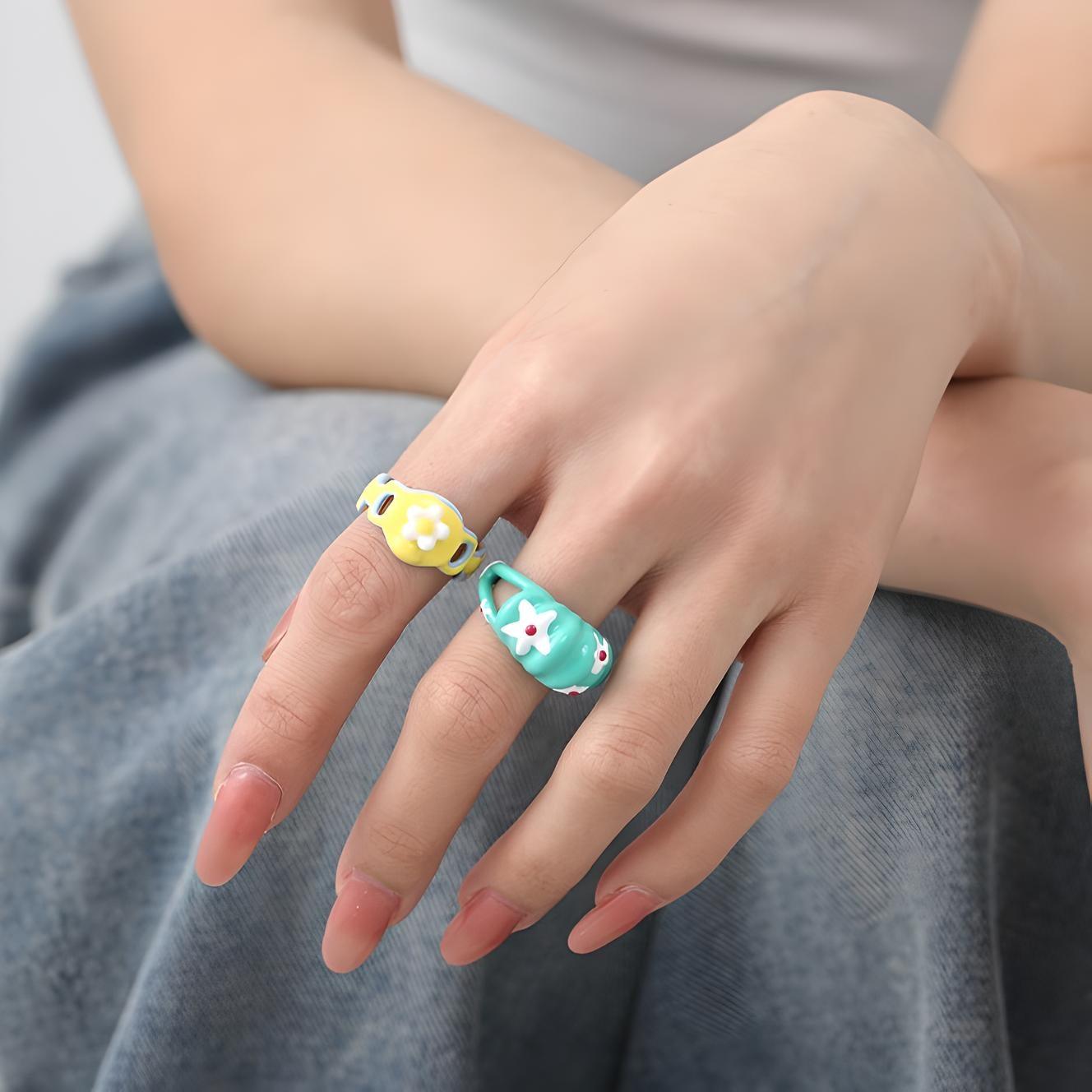 Close-up of a hand with colorful, cute animal-themed rings against a casual attire backdrop, highlighting trendy, playful fashion accessories.