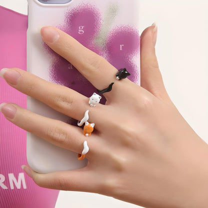 Close-up of a hand with cute cat-shaped rings holding a smartphone, showcasing whimsical jewelry and mobile accessory style.