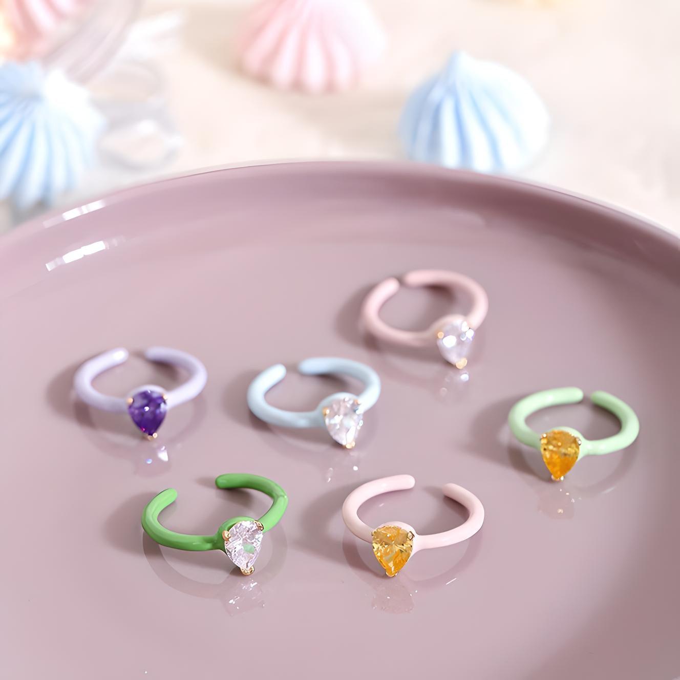 Colorful heart-shaped gemstone rings displayed on a pastel plate with merengue kisses in the background, capturing a whimsical, romantic aesthetic. Perfect for fashion and jewelry enthusiasts.