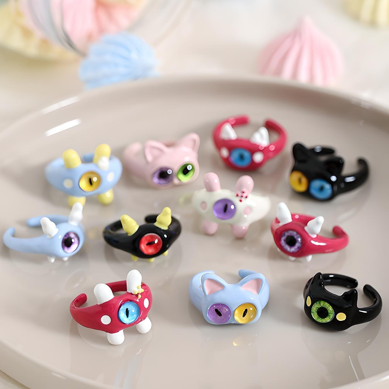 Collection of colorful, whimsical cat ring holders displayed on a plate with meringues, perfect for quirky jewelry organization and cat enthusiasts.