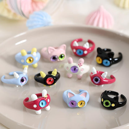 Collection of colorful, whimsical cat ring holders displayed on a plate with meringues, perfect for quirky jewelry organization and cat enthusiasts.