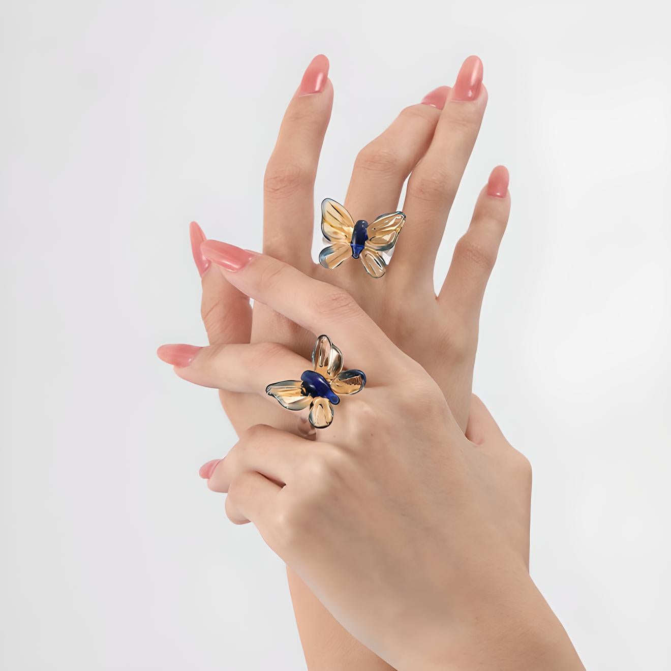 Elegant hands with pink manicure showcase gold butterfly rings with sapphire accents, embodying sophistication and style on a clean white background. Perfect for fashion accessories branding.