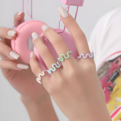 Woman with chic French manicure wearing trendy spiral rings, adjusting stylish pink headphones, showcasing modern fashion and tech accessories. Perfect for fashion and lifestyle content.