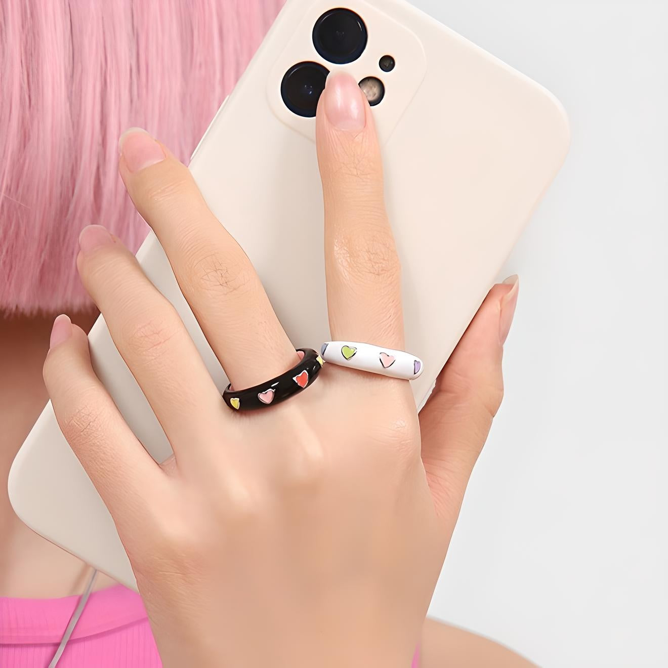 Person holding smartphone, showcasing stylish heart-patterned rings against a minimalist backdrop, perfect for modern fashion accessory marketing.