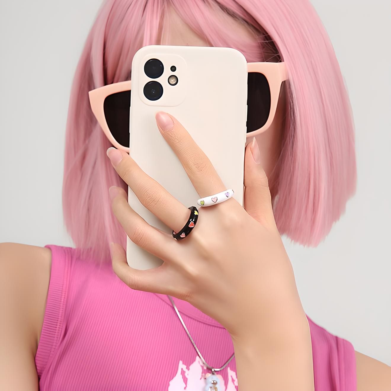 Person with pink hair and sunglasses holding a smartphone, showcasing trendy accessories and tech gadgets.